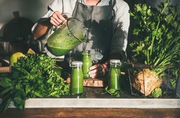 Woman in apron pouring green smoothie from blender to bottle